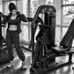 Frau steht im Gym zwischen Krafttrainingsgeräten und bereitet sich auf ihr Training vor.