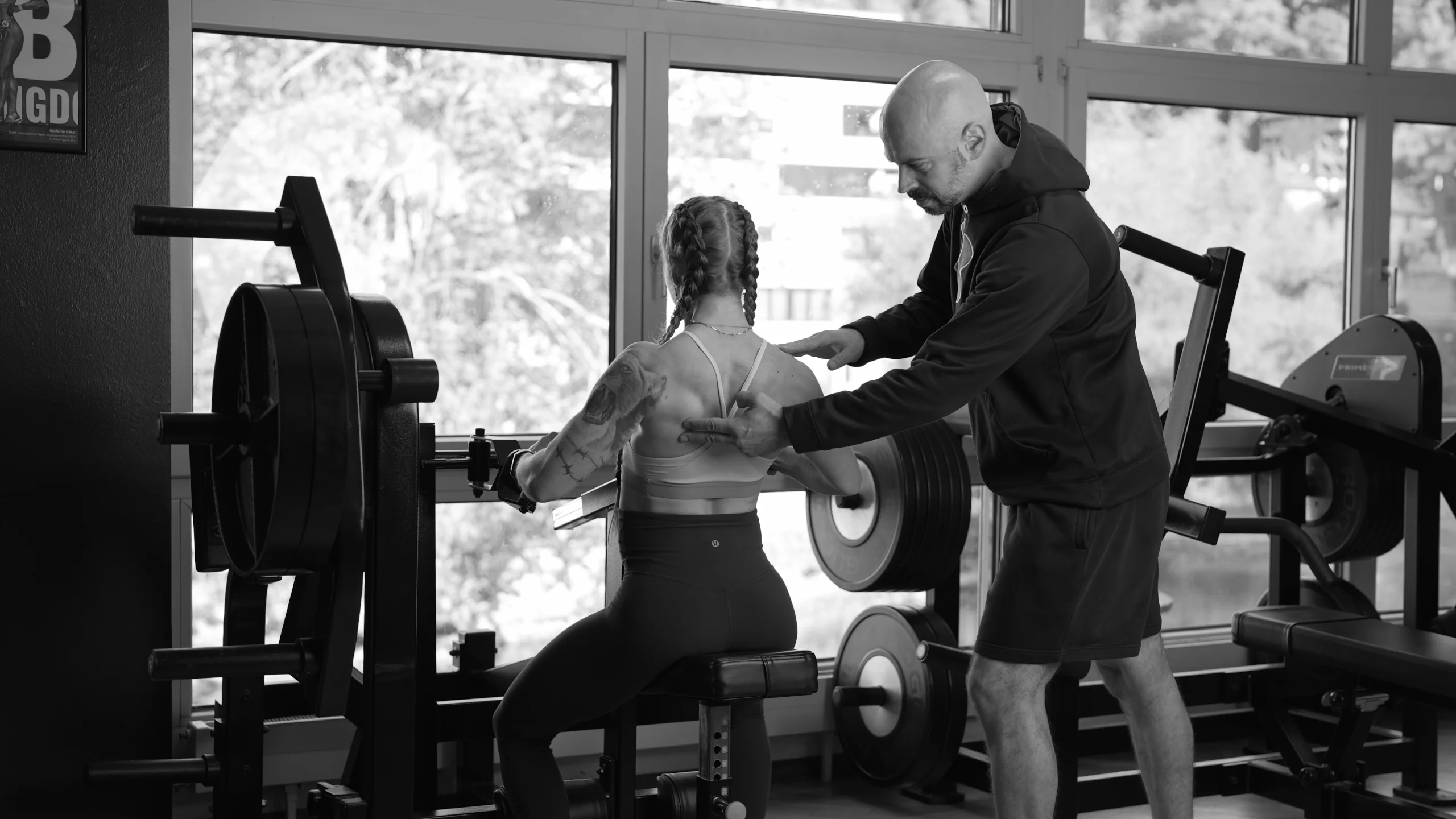 athletin-ruderzug-bikini-athletin-coach-semper-fi-body-concept Eine Frau trainiert an der Rudermaschine. Der Coach erklärt ihr, auf welche Muskeln sie sich konzentrieren soll.