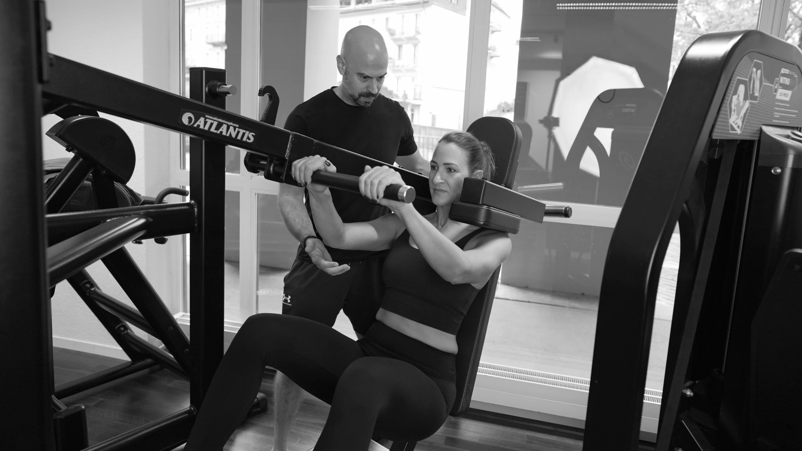frau-pendulum-squat-mit-coach-semper-fi-body-concept-personal-trainer-baden Eine Frau macht Kniebeugen an der Pendulum Squat Maschine. Der Coach spottet sie.