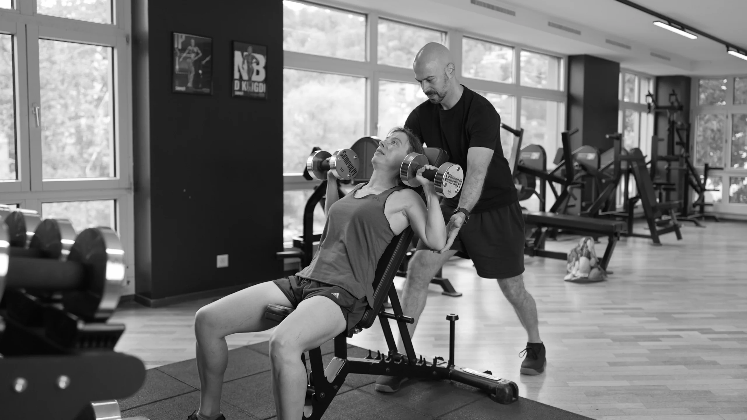 frau-schulterdruecken-mit-coach-semper-fi-body-concept-personal-trainer-baden Eine Frau macht Schulterdrücken mit Kurzhanteln. Der Coach steht hinter ihr und gibt ihr Support.