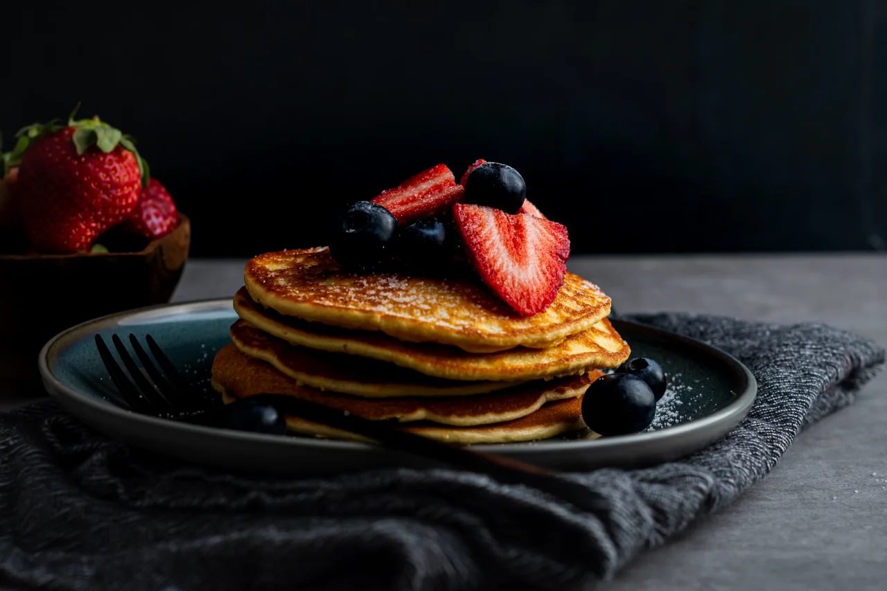 High Protein Pancakes garniert mit Erdbeeren und Heidelbeeren, angerichtet auf einem Teller.