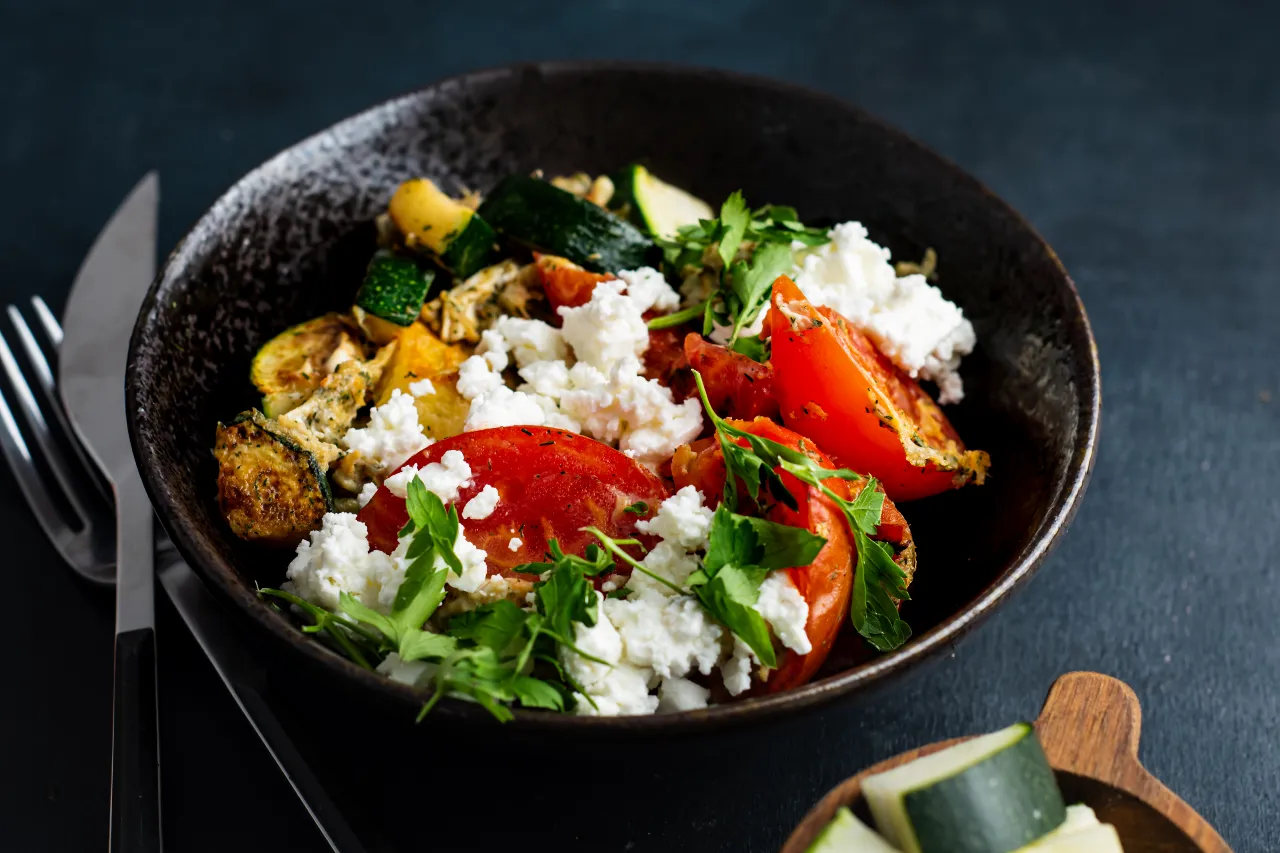 Rührei mit Fetakäse, Tomate und Zucchini, angerichtet in einer Schale.